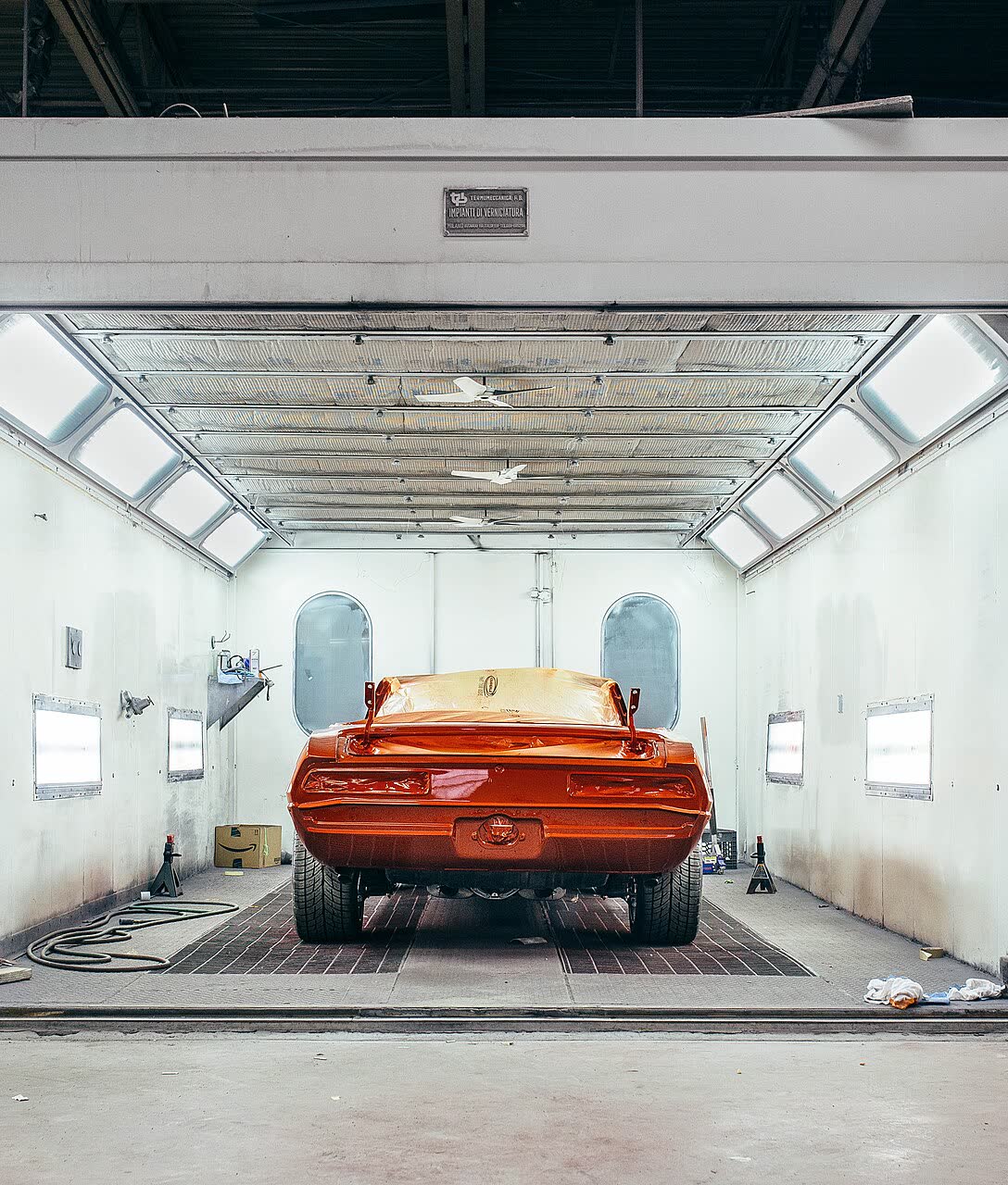 Carro esportivo laranja dentro de uma cabine de pintura branca e iluminada, visto de trás