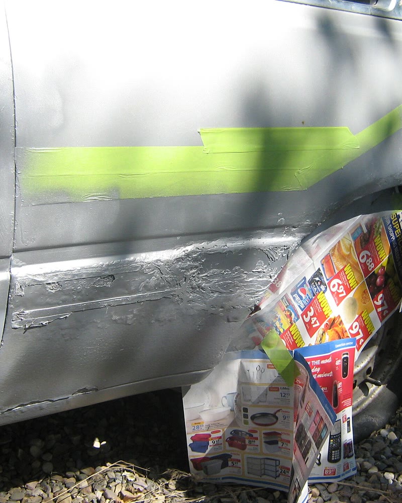 Lateral de carro prata com uma peça nova soldada e massa por lixar, protegida com jornal