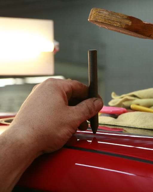 Mão apoiando uma ferramenta de metal na borda do teto de um carro vermelho