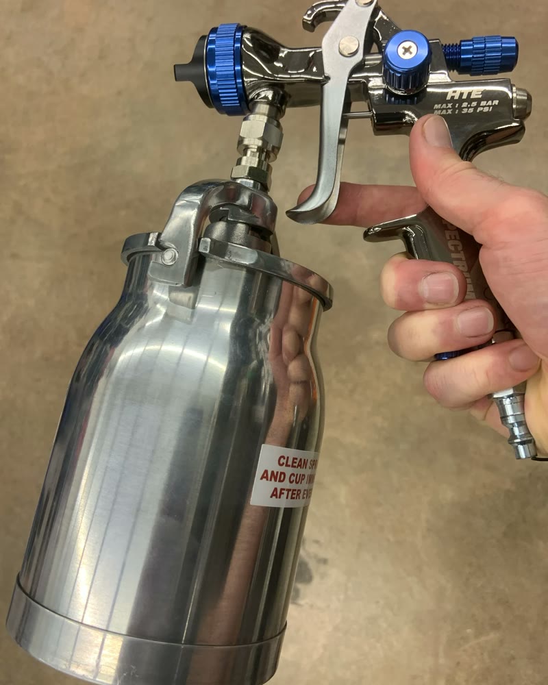 Mão segurando uma pistola de pintura com caneca de alumínio
